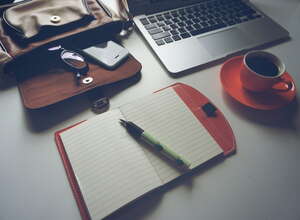Laptop, Notizbuch, Kaffeetasse und Tasche auf einem weißen Tisch